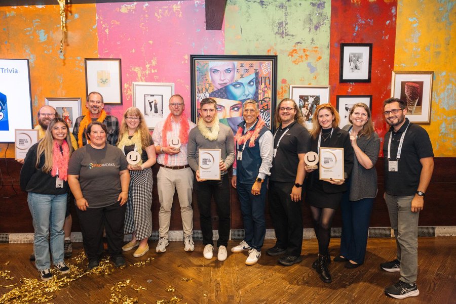Group photo of award recipients holding trophies and framed certificates in front of a colorful mural wall.