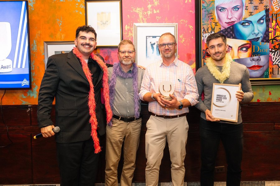 Four people at the awards reception, one holding the trophy and one holding the framed American Standout Award certificate.